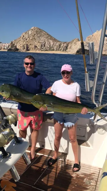 Couple holding two mahi-mahi (dorado) by the Arch of Cabo San Lucas on a sportfishing charter